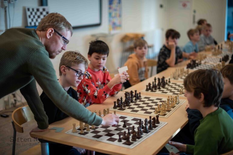 Billedet er af en voksen og børn der spiller skak på Præstemarkskolen til skolernes skakdag 2024